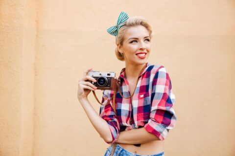 Beautiful cheerful pinup girl in yellow dress using vintage camera